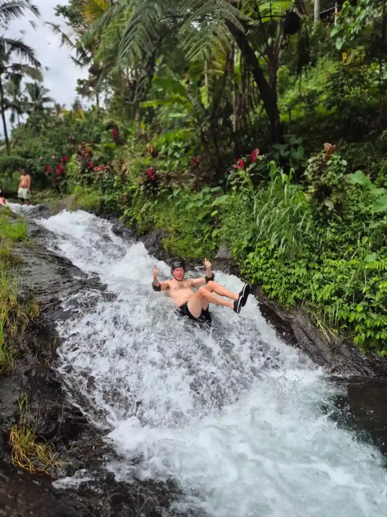 Tamu bule bersiap meluncur di Waterslide Lemukih Bali dengan latar air terjun alami yang deras
